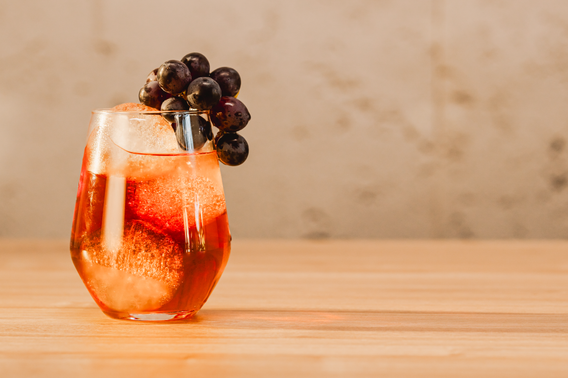 Ein elegantes Glas mit einem sprudelnden Getränk, gefüllt mit Eis und garniert mit frischen Trauben, steht auf einem Holztisch.