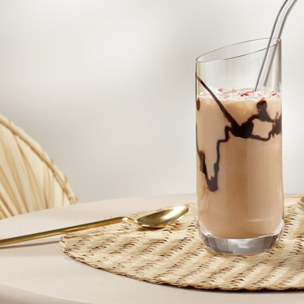 Ein elegantes Glas mit einem schokoladigen Getränk steht auf einem runden Tisch, umgeben von einer warmen, einladenden Atmosphäre.