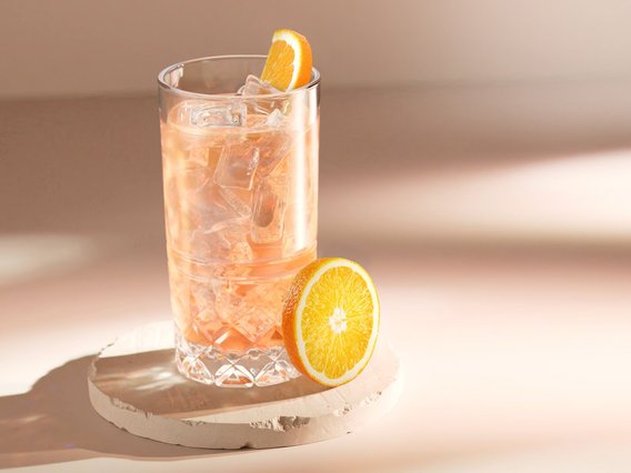 Ein Glas mit einem erfrischenden, eisgekühlten Getränk steht auf einem hellen Untergrund, garniert mit einer Orangenscheibe.