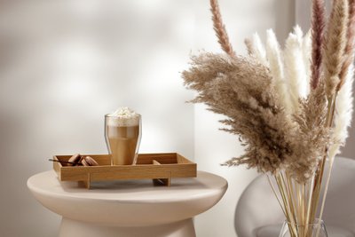 Ein Glas mit einem cremigen Getränk, garniert mit Sahne, steht auf einem Holztablett neben köstlichen Macarons.