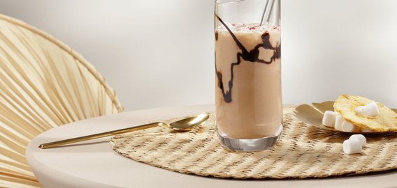Ein elegantes Glas mit einem schokoladigen Getränk steht auf einem runden Tisch, umgeben von einer warmen, einladenden Atmosphäre.