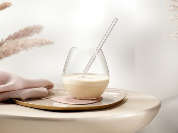 Ein elegantes Glas mit einem cremigen Getränk und einem transparenten Strohhalm steht auf einem stilvollen Untersetzer.
