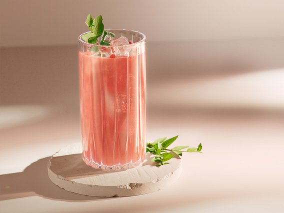 Ein rosa Getränk mit Eis und Minze, das auf einem hellen, runden Stein präsentiert wird, strahlt Sommerfrische aus.