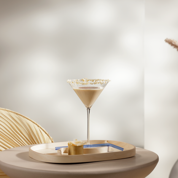 Ein eleganter Cocktail in einem Martini-Glas steht auf einem runden Tisch, umgeben von sanften, neutralen Farben.