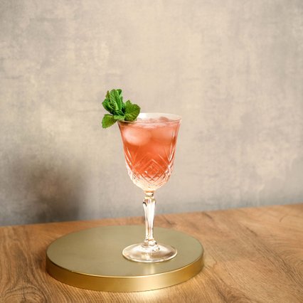 Ein eleganter Cocktail in einem Kristallglas, gefüllt mit einem rosa Getränk und dekoriert mit frischer Minze.