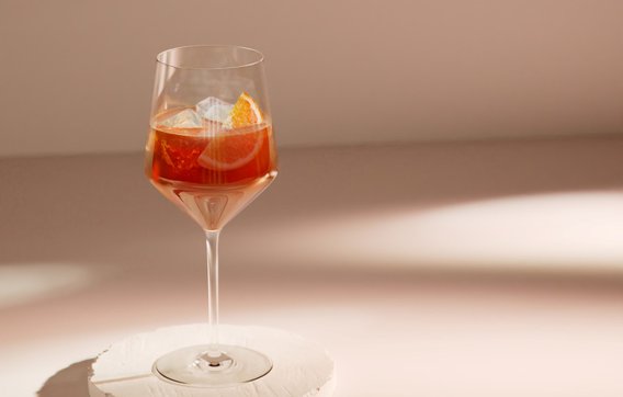 Das Glas steht auf einem weißen, runden Untersetzer und reflektiert sanftes Licht, während die orangefarbene Scheibe sichtbar ist.