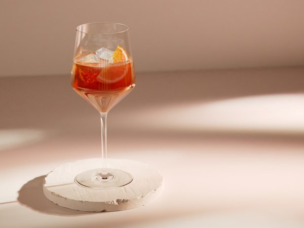 Das Glas steht auf einem weißen, runden Untersetzer und reflektiert sanftes Licht, während die orangefarbene Scheibe sichtbar ist.