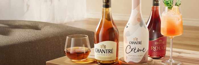 Auf einem Holztisch stehen drei Flaschen Chantré und ein Glas mit einem erfrischenden Cocktail, dekoriert mit Minze.