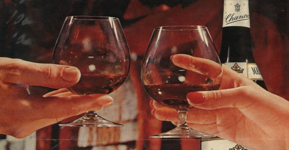 Die Hände von zwei Personen, die sich beim Anstoßen mit eleganten Gläsern begegnen, während eine Flasche im Hintergrund steht.