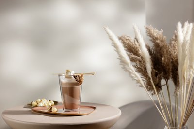 Ein elegantes Glas mit heißer Schokolade, garniert mit einem Marshmallow und Schokolade, steht auf einem runden Tisch.