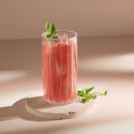 Ein stilvolles Glas mit einem pinken Cocktail, das auf einem runden, hellen Untersetzer steht, umgeben von sanften Lichtschatten.