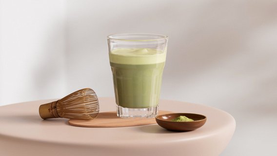 Auf einem sanften, runden Tisch befindet sich ein Glas mit grünem Matcha und eine kleine Schale mit Matcha-Pulver.