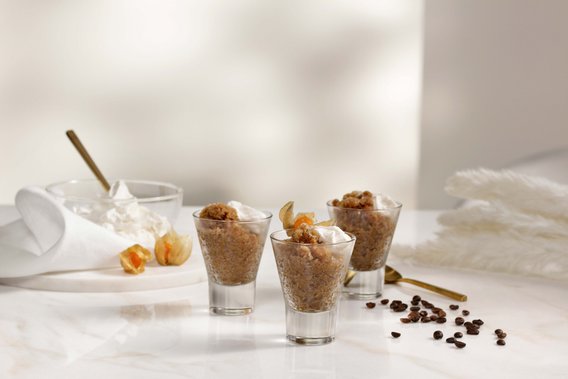 Drei Gläser mit einer cremigen Dessertschicht, garniert mit Sahne und einer Frucht, stehen auf einem eleganten Tisch.