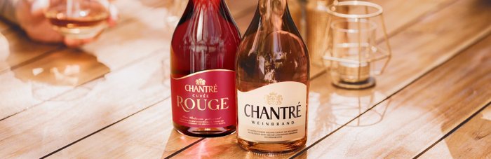 Zwei Flaschen CHANTRÉ stehen auf einem Holztisch, eine mit rotem Etikett und die andere mit einem hellen, eleganten Design.