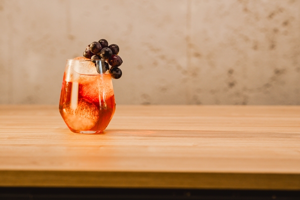 Ein elegantes Glas mit einem sprudelnden Getränk, gefüllt mit Eis und garniert mit frischen Trauben, steht auf einem Holztisch.