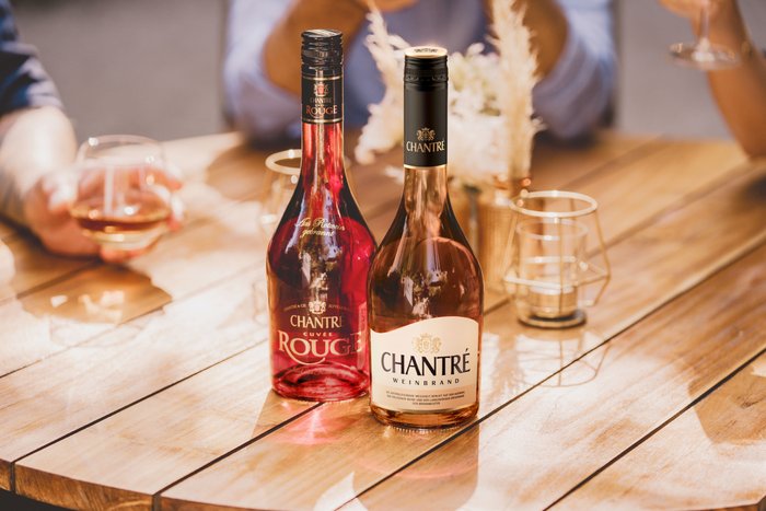 Auf einem sonnigen Tisch liegen zwei Flaschen Chantré, eine rote und eine roséfarbene, neben Gläsern und einer stilvollen Deko.
