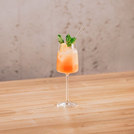 Ein elegantes Glas mit einem erfrischenden, orangefarbenen Cocktail steht auf einem hellen Holztisch.