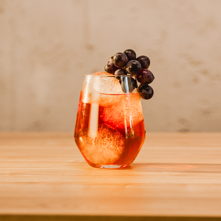 Ein elegantes Glas mit einem sprudelnden Getränk, gefüllt mit Eis und garniert mit frischen Trauben, steht auf einem Holztisch.