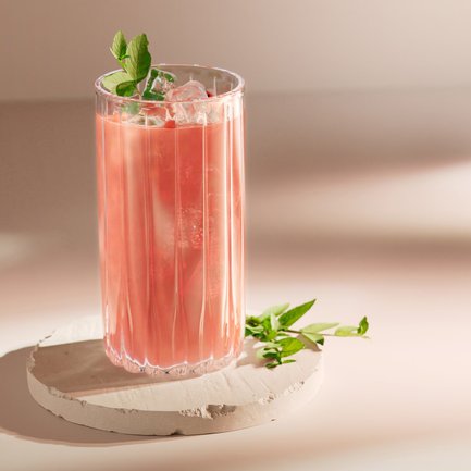 Ein rosa Getränk mit Eis und Minze, das auf einem hellen, runden Stein präsentiert wird, strahlt Sommerfrische aus.