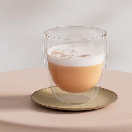 Das Glas zeigt eine Schichtung aus hellbraunem Getränk und schaumiger Oberseite, umgeben von einem sanften Hintergrund.