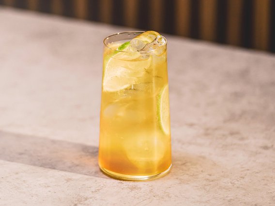 Ein erfrischendes Getränk in einem hohen Glas, gefüllt mit Eiswürfeln und einer Limettenscheibe, auf einem hellen Tisch.