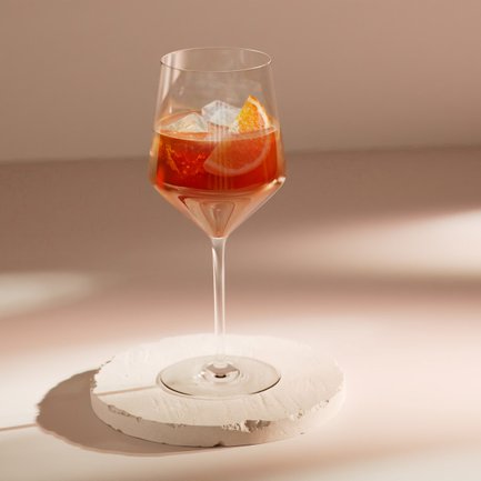 Das Glas steht auf einem weißen, runden Untersetzer und reflektiert sanftes Licht, während die orangefarbene Scheibe sichtbar ist.