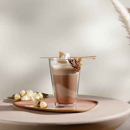 Ein elegantes Glas mit heißer Schokolade, garniert mit einem Marshmallow und Schokolade, steht auf einem runden Tisch.