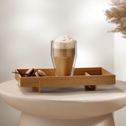 Ein Glas mit einem cremigen Getränk, garniert mit Sahne, steht auf einem Holztablett neben köstlichen Macarons.
