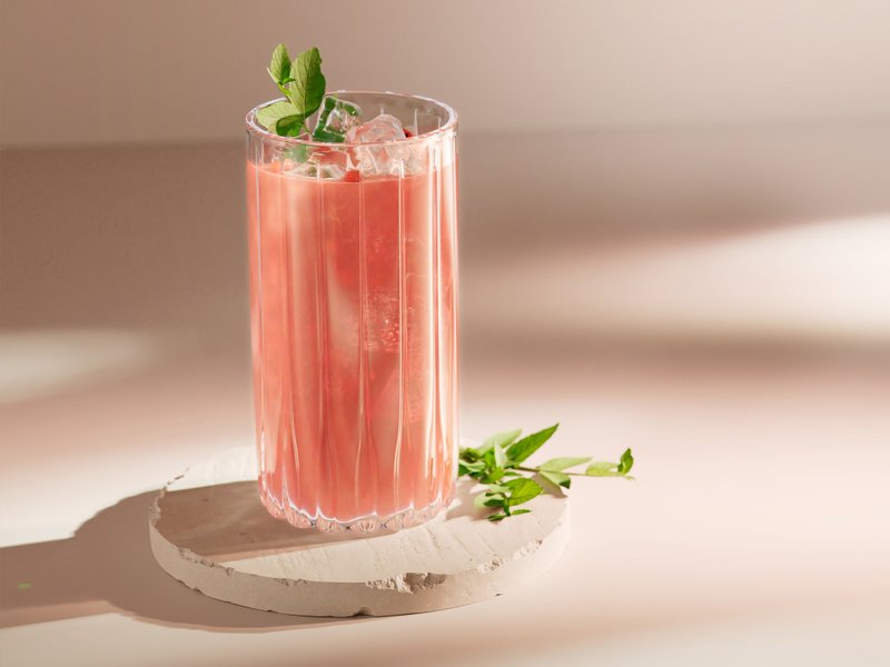 Ein rosa Getränk mit Eis und Minze, das auf einem hellen, runden Stein präsentiert wird, strahlt Sommerfrische aus.