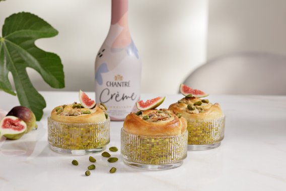 Drei dekorative Dessertschalen mit Pistazien und Feigenstücken, umgeben von frischen Feigen und einem Flasche Chantre Crème.