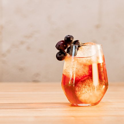 Das Glas mit einem prickelnden Getränk und Eiswürfeln wird von saftigen Trauben gekrönt und steht auf einer Holzoberfläche.