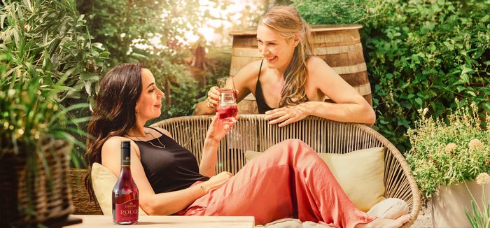 Zwei Frauen genießen einen entspannten Moment im Freien, während sie fruchtige Getränke in der Hand halten und lachen.