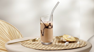 Ein elegantes Glas mit einem schokoladigen Getränk steht auf einem runden Tisch, umgeben von einer warmen, einladenden Atmosphäre.