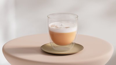 Das Glas zeigt eine Schichtung aus hellbraunem Getränk und schaumiger Oberseite, umgeben von einem sanften Hintergrund.