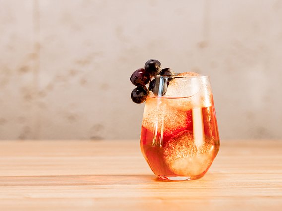 Das Glas mit einem prickelnden Getränk und Eiswürfeln wird von saftigen Trauben gekrönt und steht auf einer Holzoberfläche.