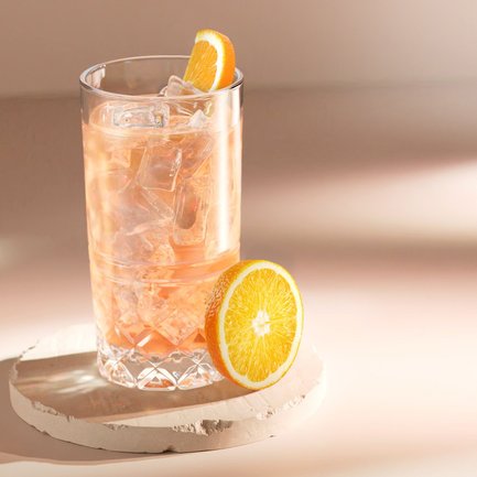 Ein Glas mit einem erfrischenden, eisgekühlten Getränk steht auf einem hellen Untergrund, garniert mit einer Orangenscheibe.