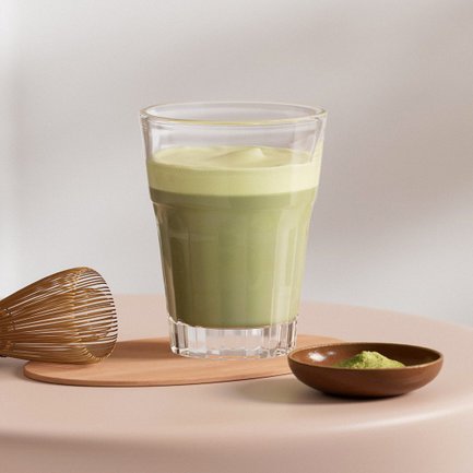 Auf einem sanften, runden Tisch befindet sich ein Glas mit grünem Matcha und eine kleine Schale mit Matcha-Pulver.