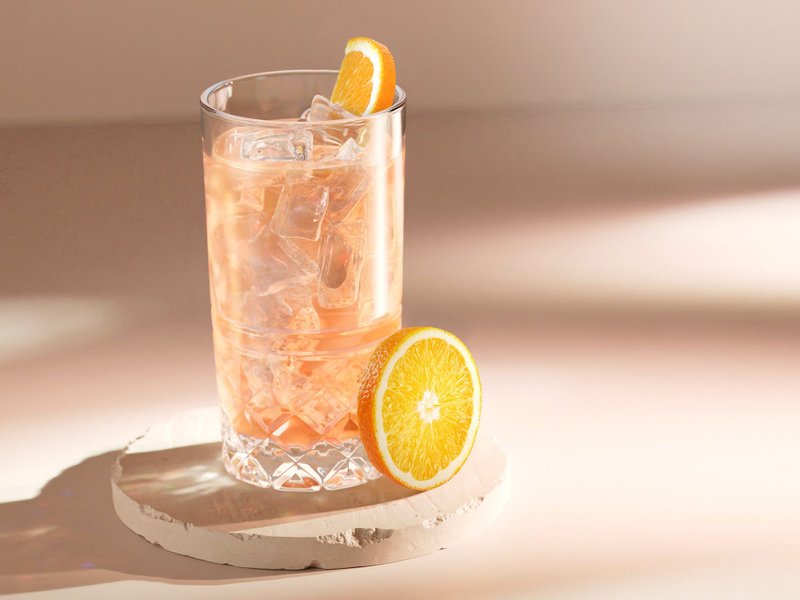 Ein Glas mit einem erfrischenden, eisgekühlten Getränk steht auf einem hellen Untergrund, garniert mit einer Orangenscheibe.