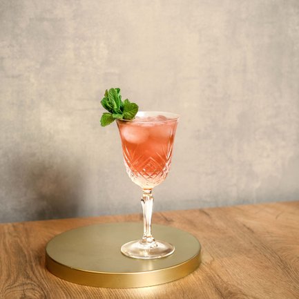 Ein eleganter Cocktail in einem Kristallglas, gefüllt mit einem rosa Getränk und dekoriert mit frischer Minze.