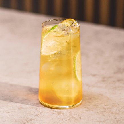 Ein erfrischendes Getränk in einem hohen Glas, gefüllt mit Eiswürfeln und einer Limettenscheibe, auf einem hellen Tisch.