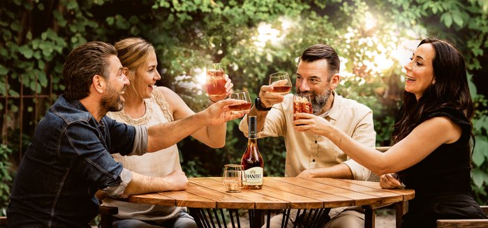 Vier Freunde stoßen fröhlich mit Getränken an, umgeben von üppigem Grün und einer warmen, einladenden Atmosphäre.