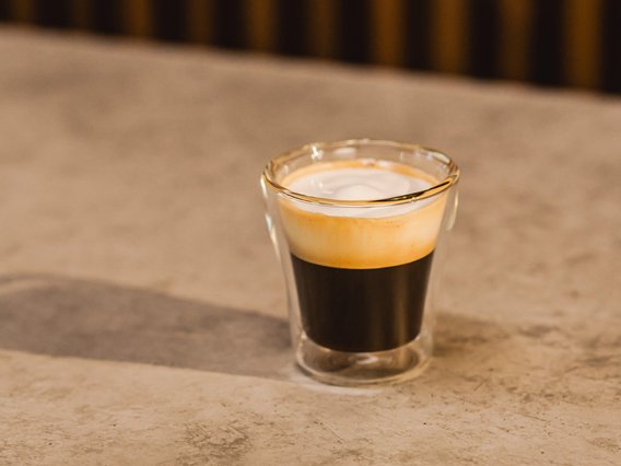 Das Glas zeigt eine perfekt geschichtete Espresso-Kreation, mit dunklem Kaffee und einer hellen, schaumigen Krone.