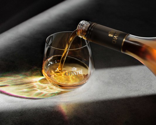 Ein Glas wird mit einem goldenen Getränk gefüllt, während Lichtreflexionen auf der Oberfläche sichtbar sind.