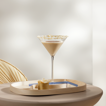 Ein eleganter Cocktail in einem Martini-Glas steht auf einem runden Tisch, umgeben von sanften, neutralen Farben.