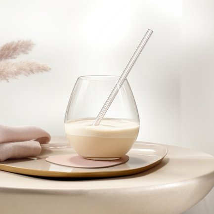 Ein elegantes Glas mit einem cremigen Getränk und einem transparenten Strohhalm steht auf einem stilvollen Untersetzer.