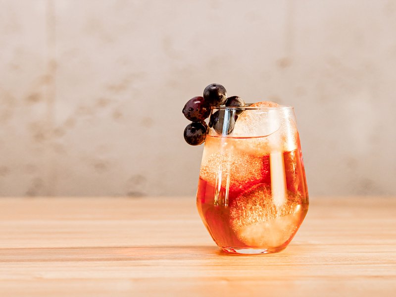 Das Glas mit einem prickelnden Getränk und Eiswürfeln wird von saftigen Trauben gekrönt und steht auf einer Holzoberfläche.