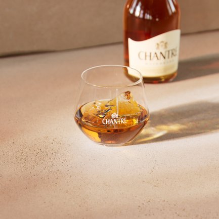 Chantré Weinbrand auf Eis im Glas, mit Flasche im Hintergrund.